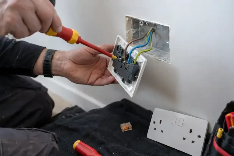 Electrician tightening a rear socket terminal with an insulated screwdriver.
